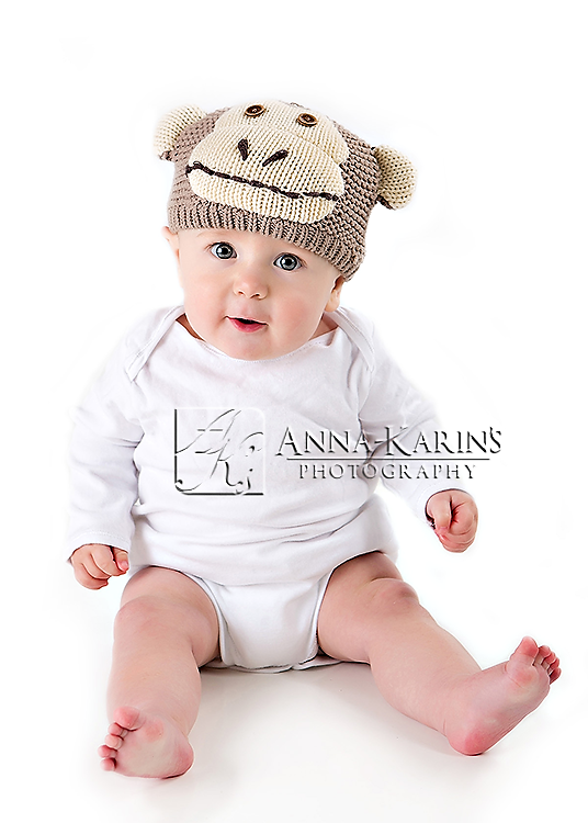 Baby with monkey hat, sitting up in white onesie, cute baby boy sitting up