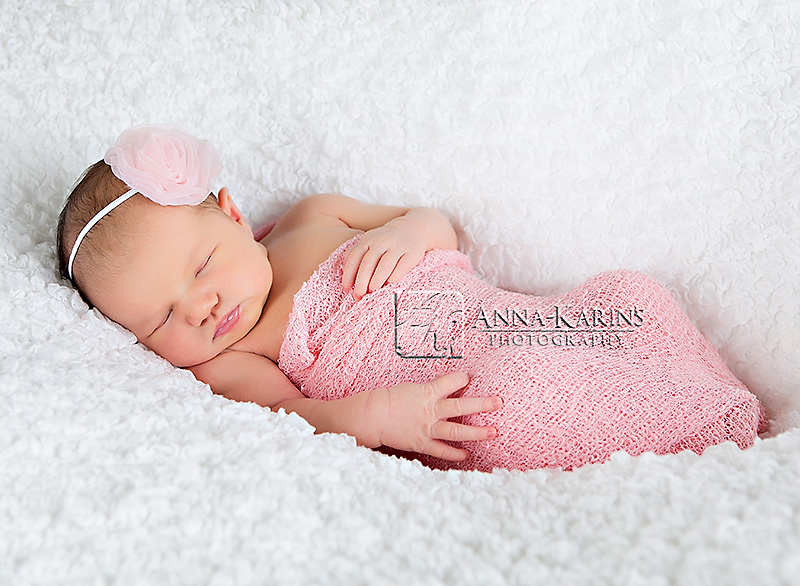 newborn baby girl in pink wrap and headband, sleepy curled up newborn baby girl